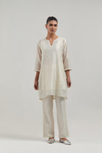 Off white silk Chanderi straight short kurta set with hand-embroidered paisley motifs with delicate mirror and sequins work at neck, hem, and sleeves, with narrow borders along the edges.