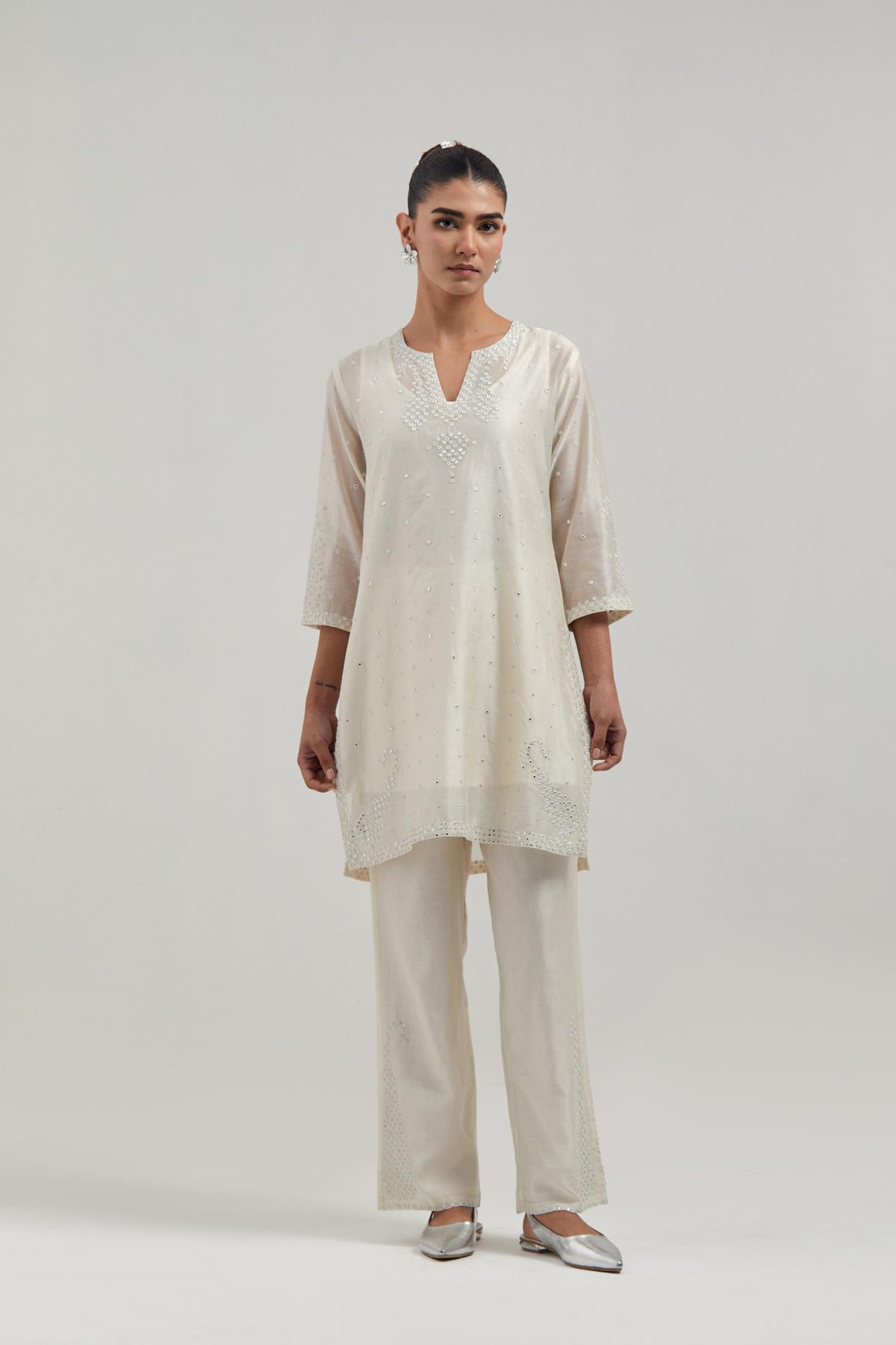 Off white silk Chanderi straight short kurta set with hand-embroidered paisley motifs with delicate mirror and sequins work at neck, hem, and sleeves, with narrow borders along the edges.