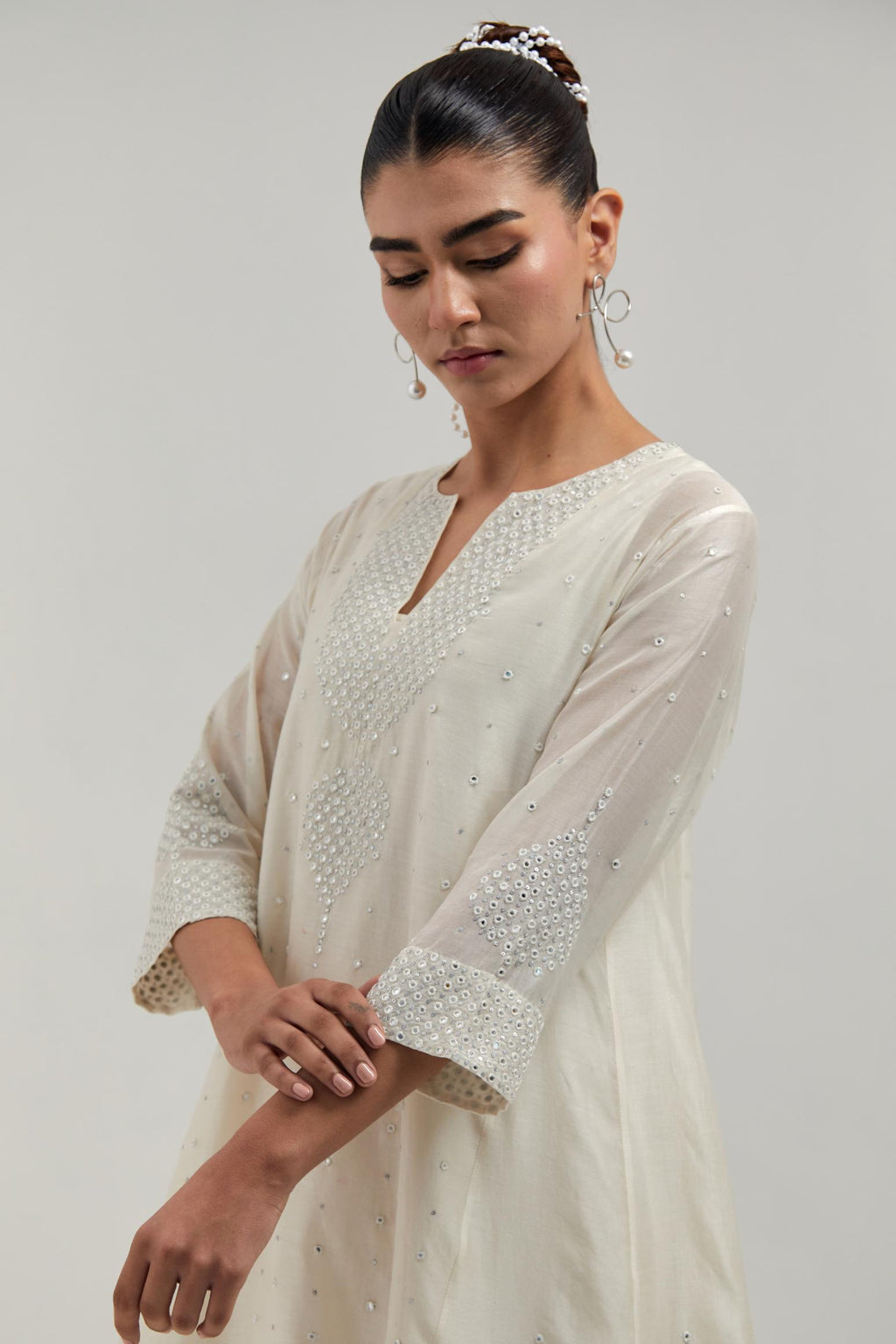 Off white silk Chanderi short kalidar kurta set, with hand embroidered mirror at neck, hem and sleeve edges, highlighted with scattered silver sequins and mirror embellishments all-over.