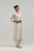 Off-white silk Chanderi straight kurta set with hand-embroidered mirror at the neck, hem and sleeves, highlighted with scattered silver sequin and mirror embellishments all-over.
