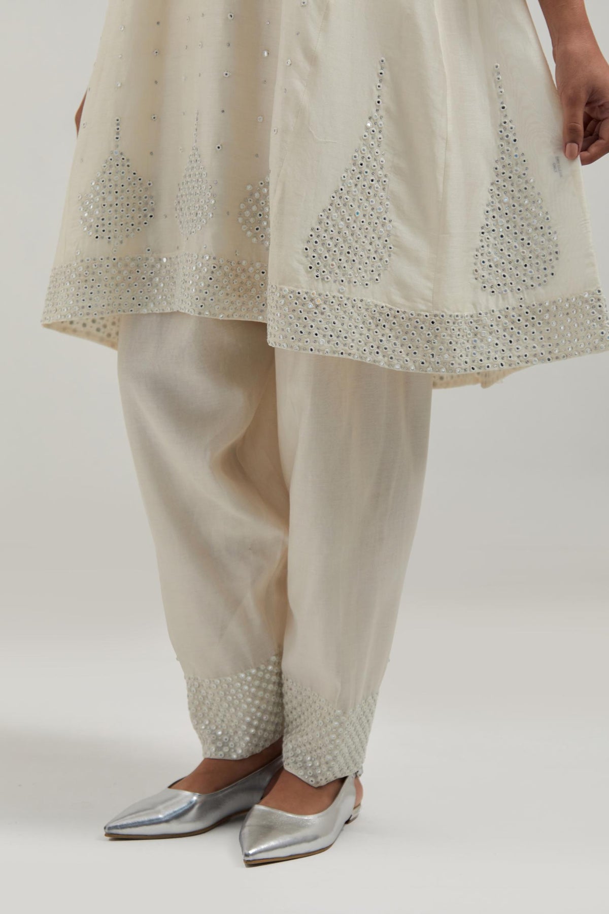 Off white silk Chanderi short kalidar kurta set, with hand embroidered mirror at neck, hem and sleeve edges, highlighted with scattered silver sequins and mirror embellishments all-over.