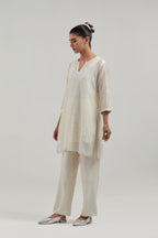 Off white silk Chanderi straight short kurta set with hand-embroidered paisley motifs with delicate mirror and sequins work at neck, hem, and sleeves, with narrow borders along the edges.