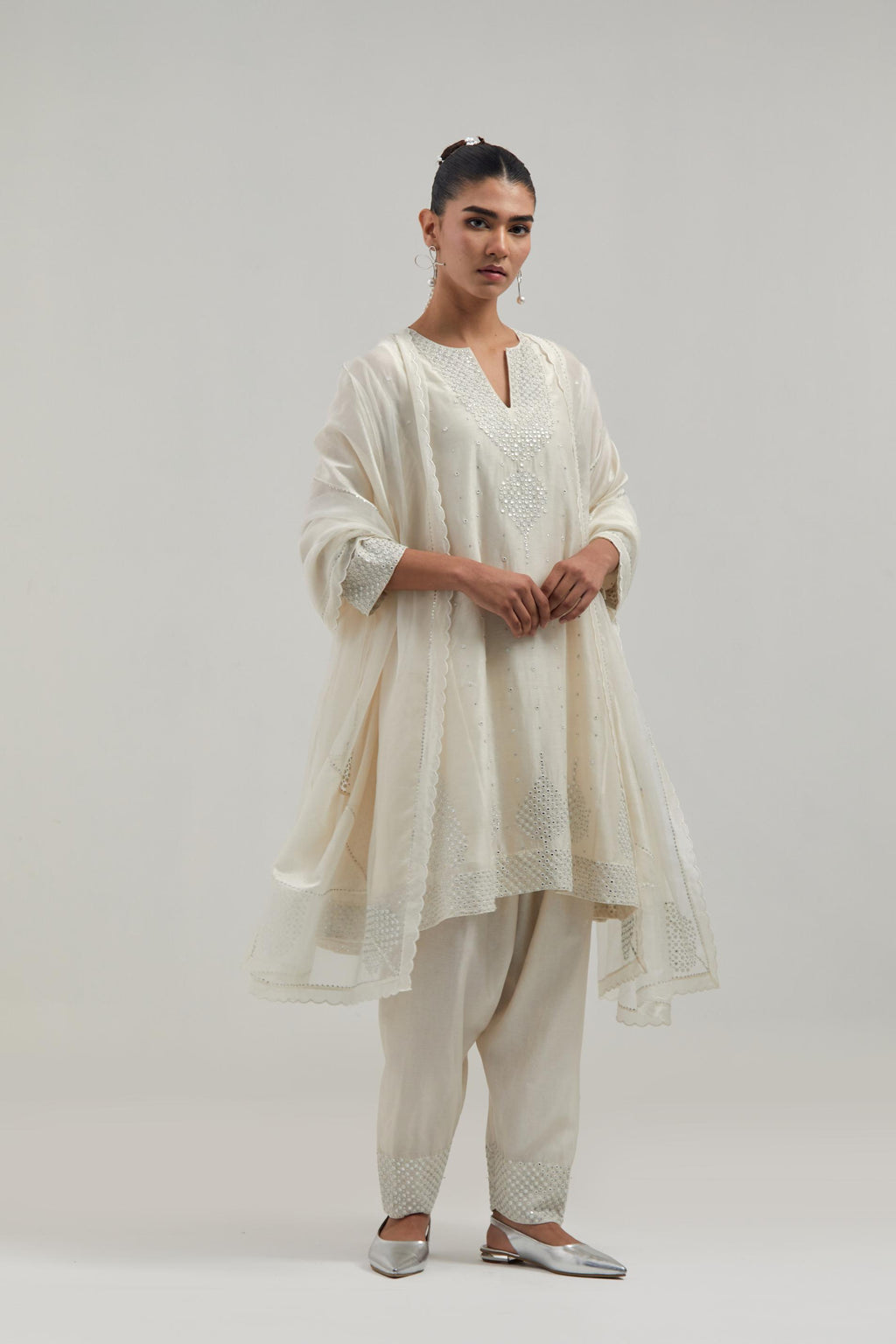 Off white silk Chanderi short kalidar kurta set, with hand embroidered mirror at neck, hem and sleeve edges, highlighted with scattered silver sequins and mirror embellishments all-over.