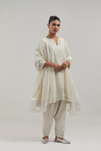 Off white silk Chanderi short kalidar kurta set, with hand embroidered mirror at neck, hem and sleeve edges, highlighted with scattered silver sequins and mirror embellishments all-over.