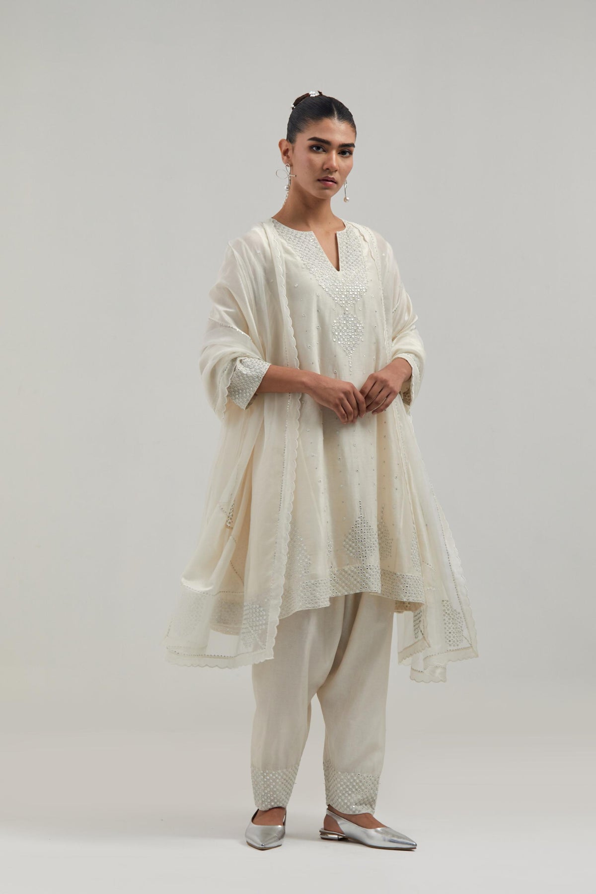 Off white silk Chanderi short kalidar kurta set, with hand embroidered mirror at neck, hem and sleeve edges, highlighted with scattered silver sequins and mirror embellishments all-over.