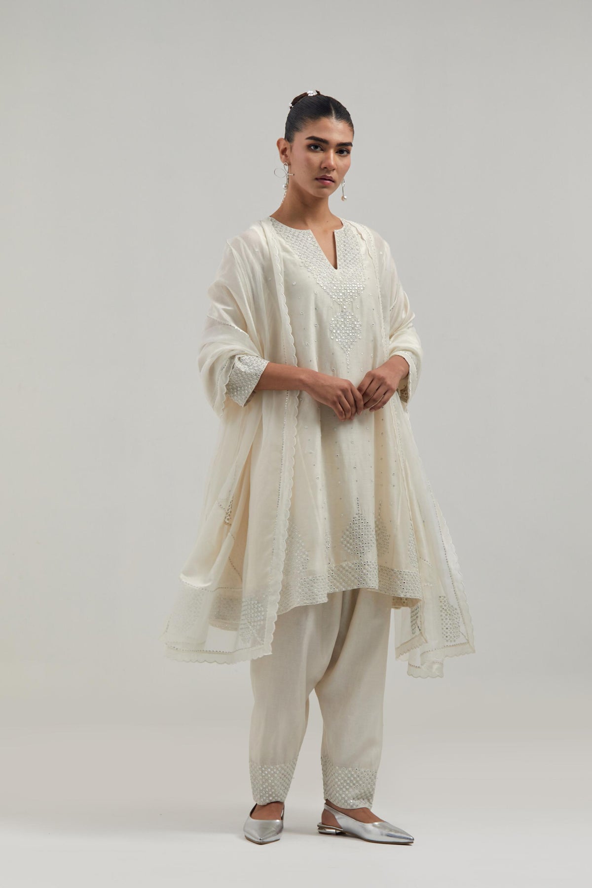 Off white silk Chanderi short kalidar kurta set, with hand embroidered mirror at neck, hem and sleeve edges, highlighted with scattered silver sequins and mirror embellishments all-over.