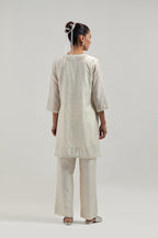 Off white silk Chanderi straight short kurta set with hand-embroidered paisley motifs with delicate mirror and sequins work at neck, hem, and sleeves, with narrow borders along the edges.