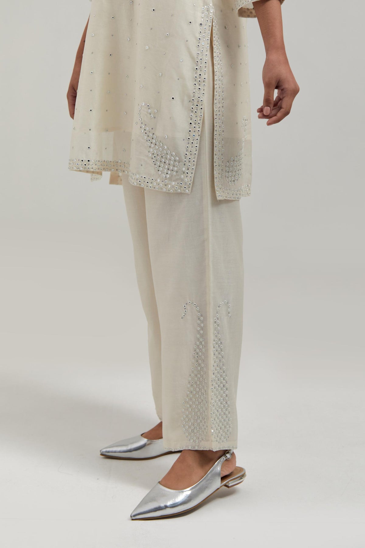 Off white silk Chanderi straight short kurta set with hand-embroidered paisley motifs with delicate mirror and sequins work at neck, hem, and sleeves, with narrow borders along the edges.