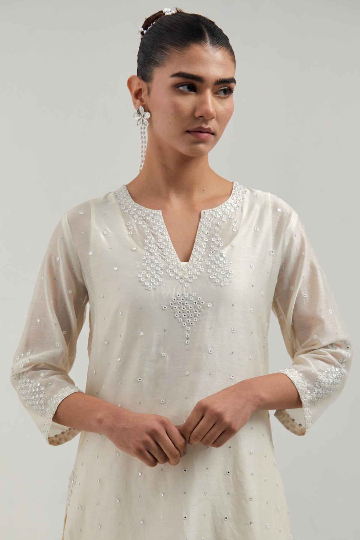 Off white silk Chanderi straight short kurta set with hand-embroidered paisley motifs with delicate mirror and sequins work at neck, hem, and sleeves, with narrow borders along the edges.