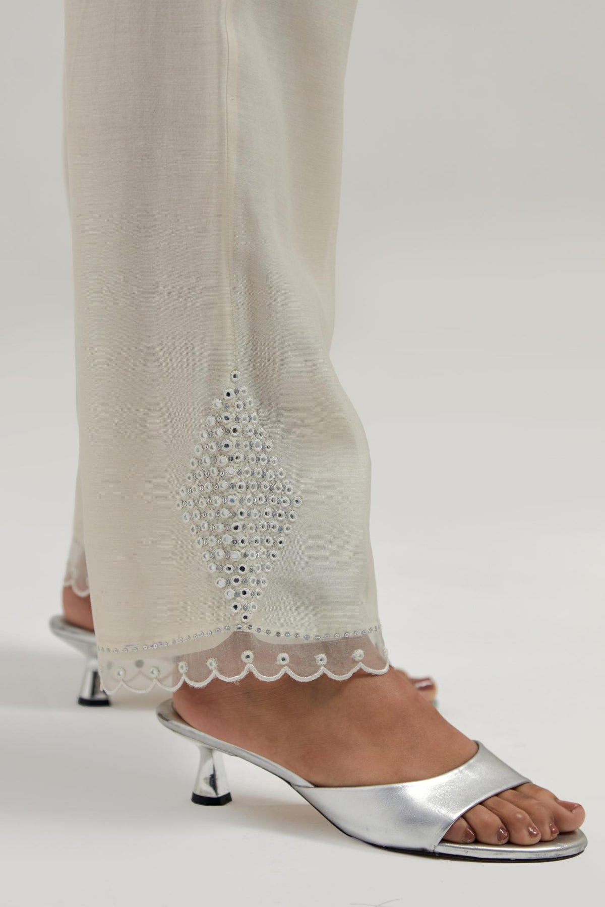 Off white silk Chanderi straight pants with narrow organza scalloped hem and hand-embroidered diamond motifs with delicate mirror & sequins work at the sides.