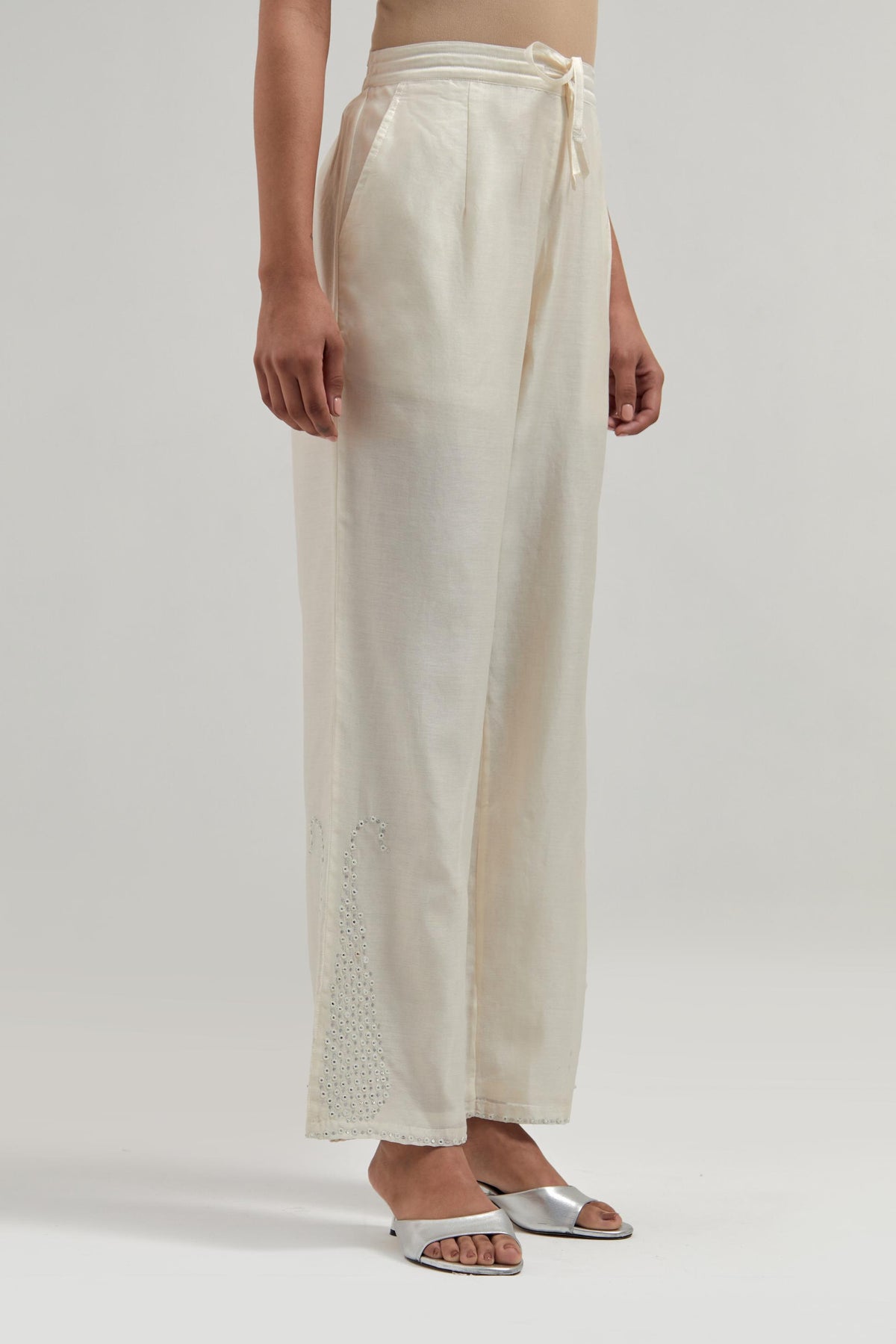 Off white silk Chanderi pants with hand-embroidered paisley motifs with delicate mirror and sequins work at the hem.
