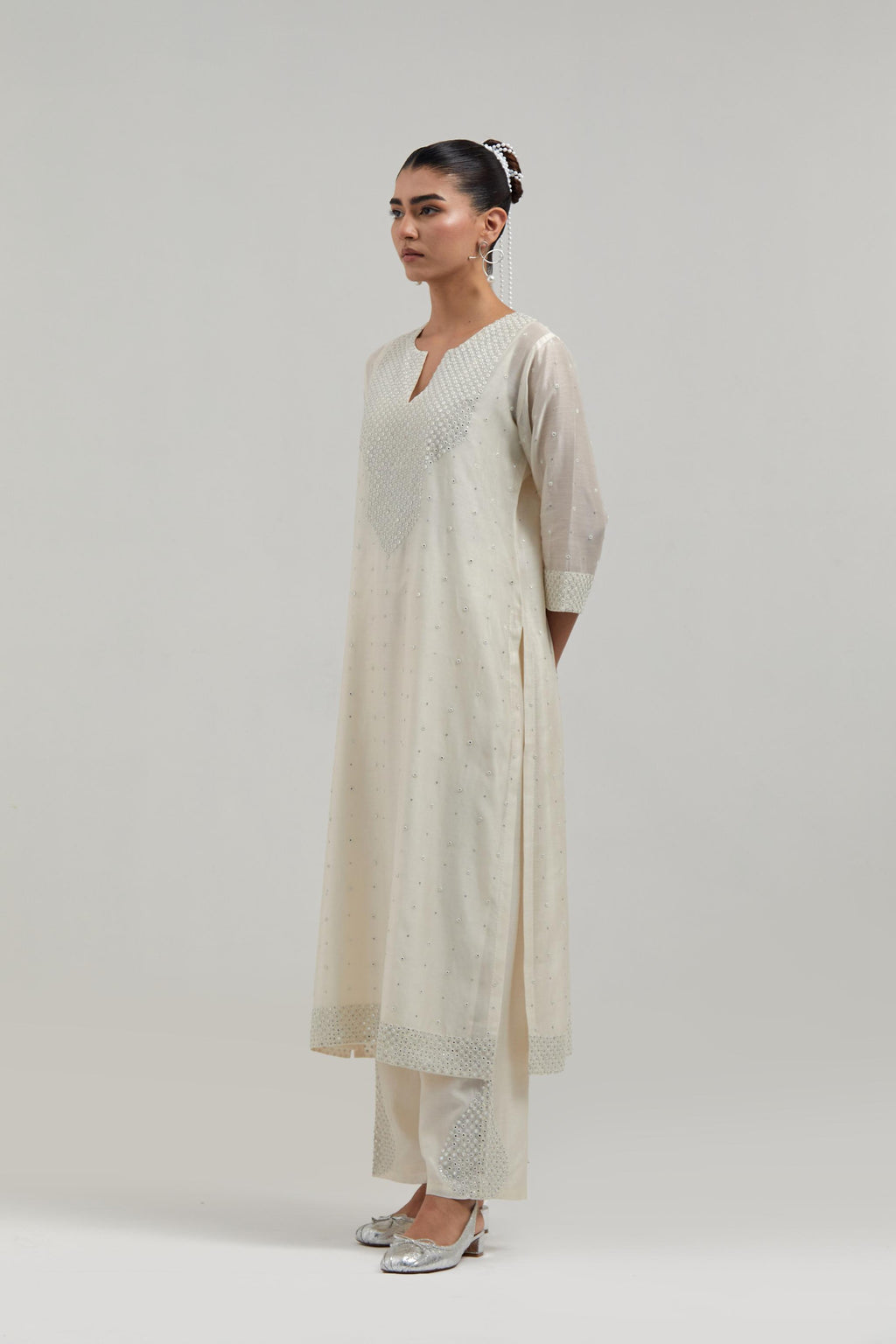 Off-white silk Chanderi straight kurta set with hand-embroidered mirror at the neck, hem and sleeves, highlighted with scattered silver sequin and mirror embellishments all-over.