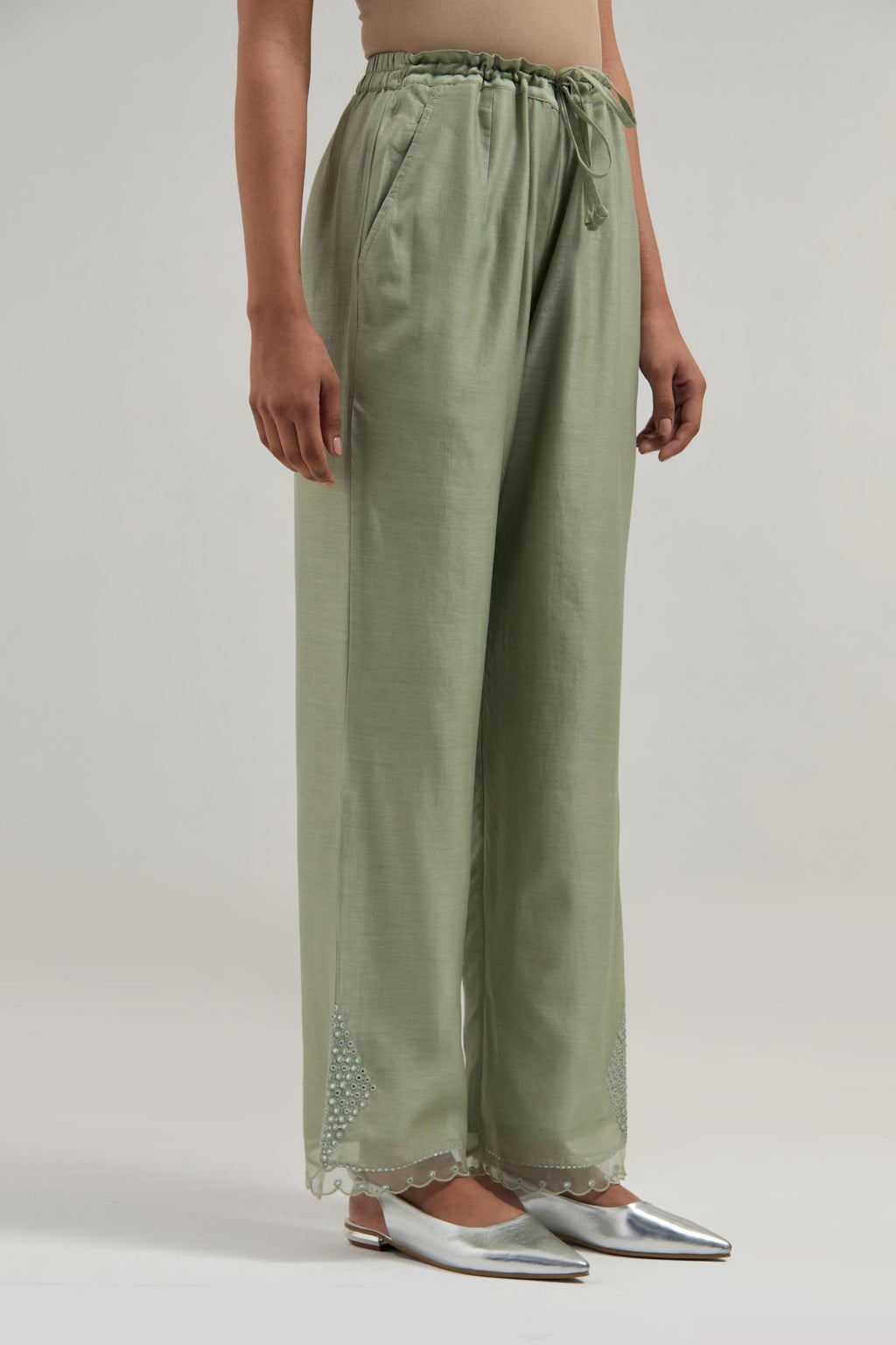 Green silk Chanderi straight pants with narrow organza scalloped hem and hand-embroidered diamond motifs with delicate mirror & sequins work at the sides.