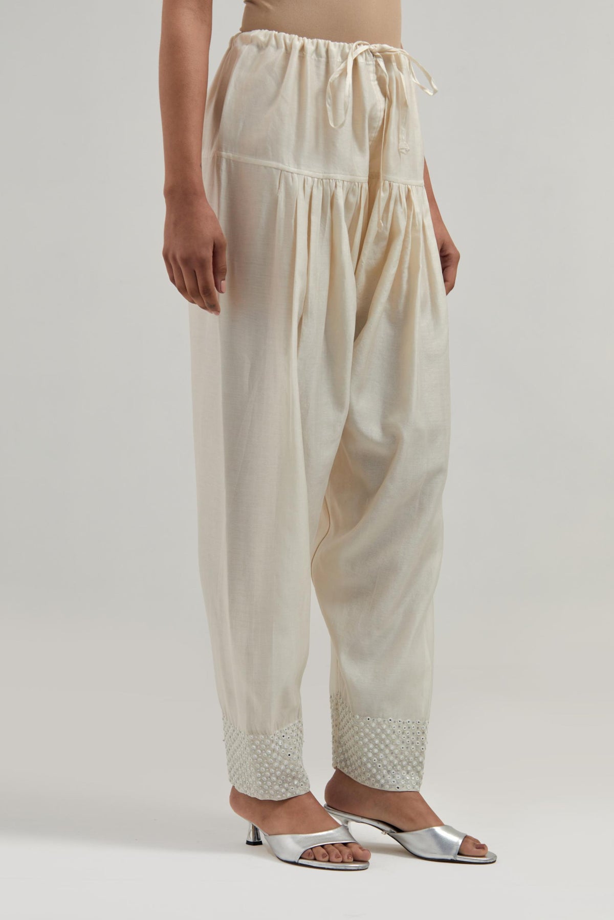 Off white silk Chanderi salwar with hand-embroidered mirror & sequins work in a broad border at the hem.