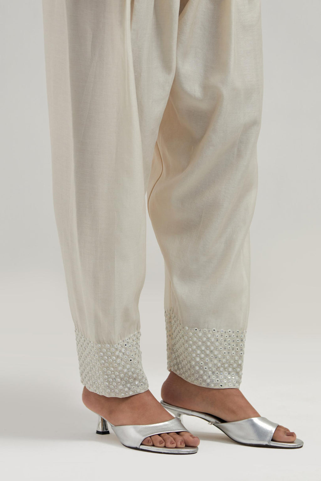 Off white silk Chanderi salwar with hand-embroidered mirror & sequins work in a broad border at the hem.