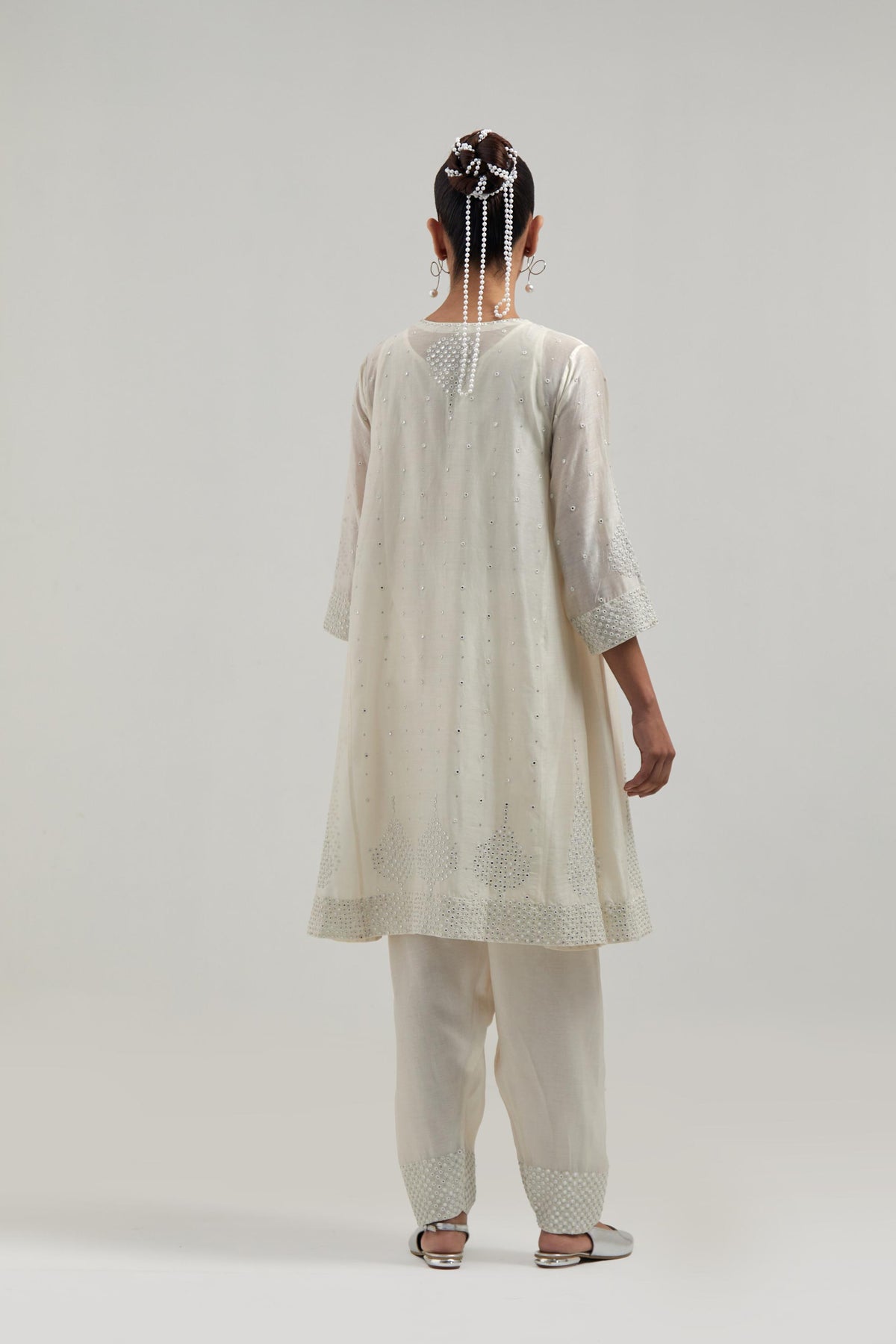 Off white silk Chanderi short kalidar kurta set, with hand embroidered mirror at neck, hem and sleeve edges, highlighted with scattered silver sequins and mirror embellishments all-over.