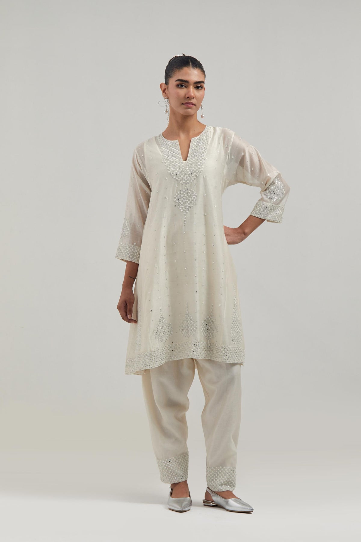 Off white silk Chanderi short kalidar kurta set, with hand embroidered mirror at neck, hem and sleeve edges, highlighted with scattered silver sequins and mirror embellishments all-over.