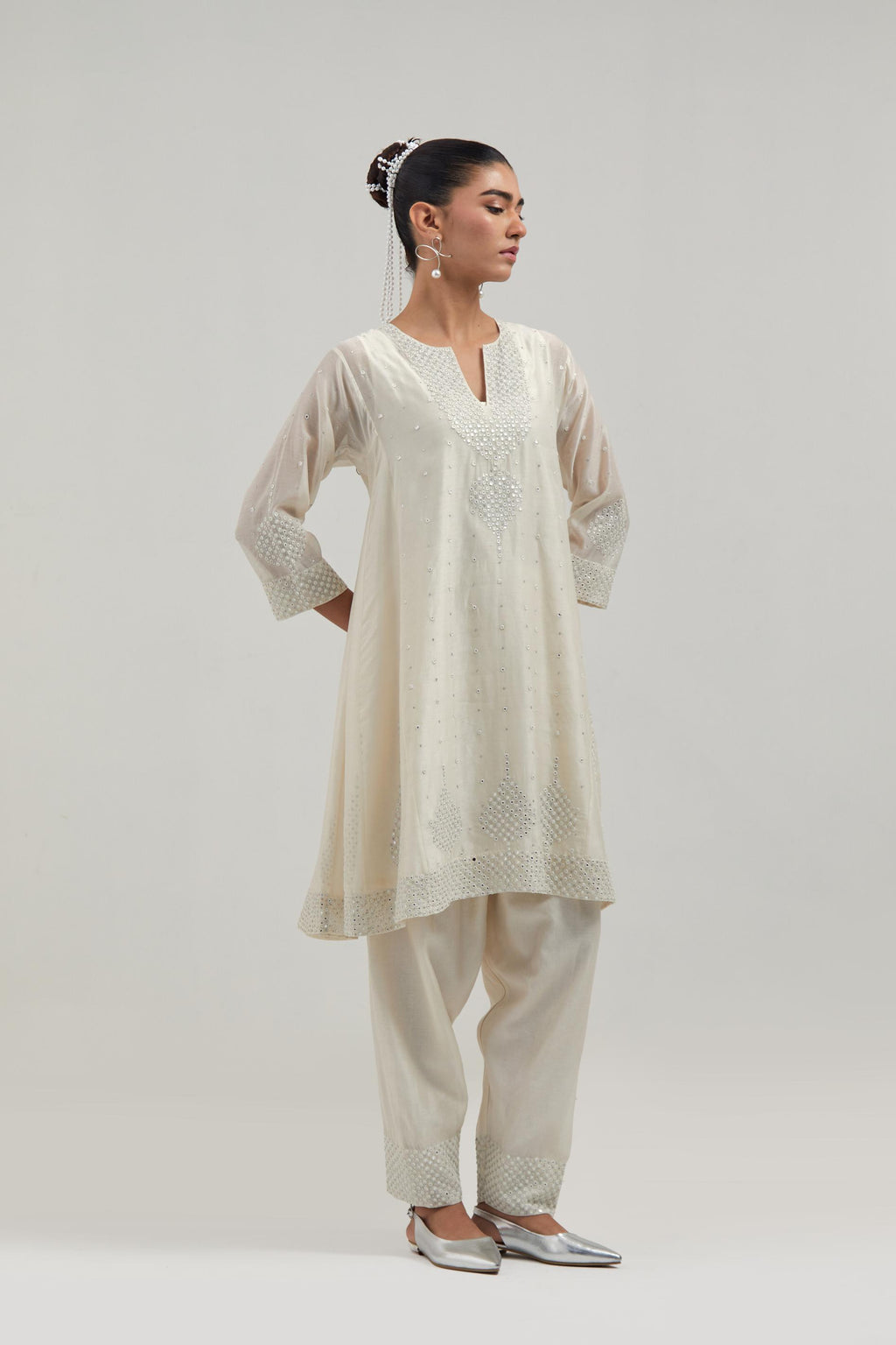 Off white silk Chanderi short kalidar kurta set, with hand embroidered mirror at neck, hem and sleeve edges, highlighted with scattered silver sequins and mirror embellishments all-over.