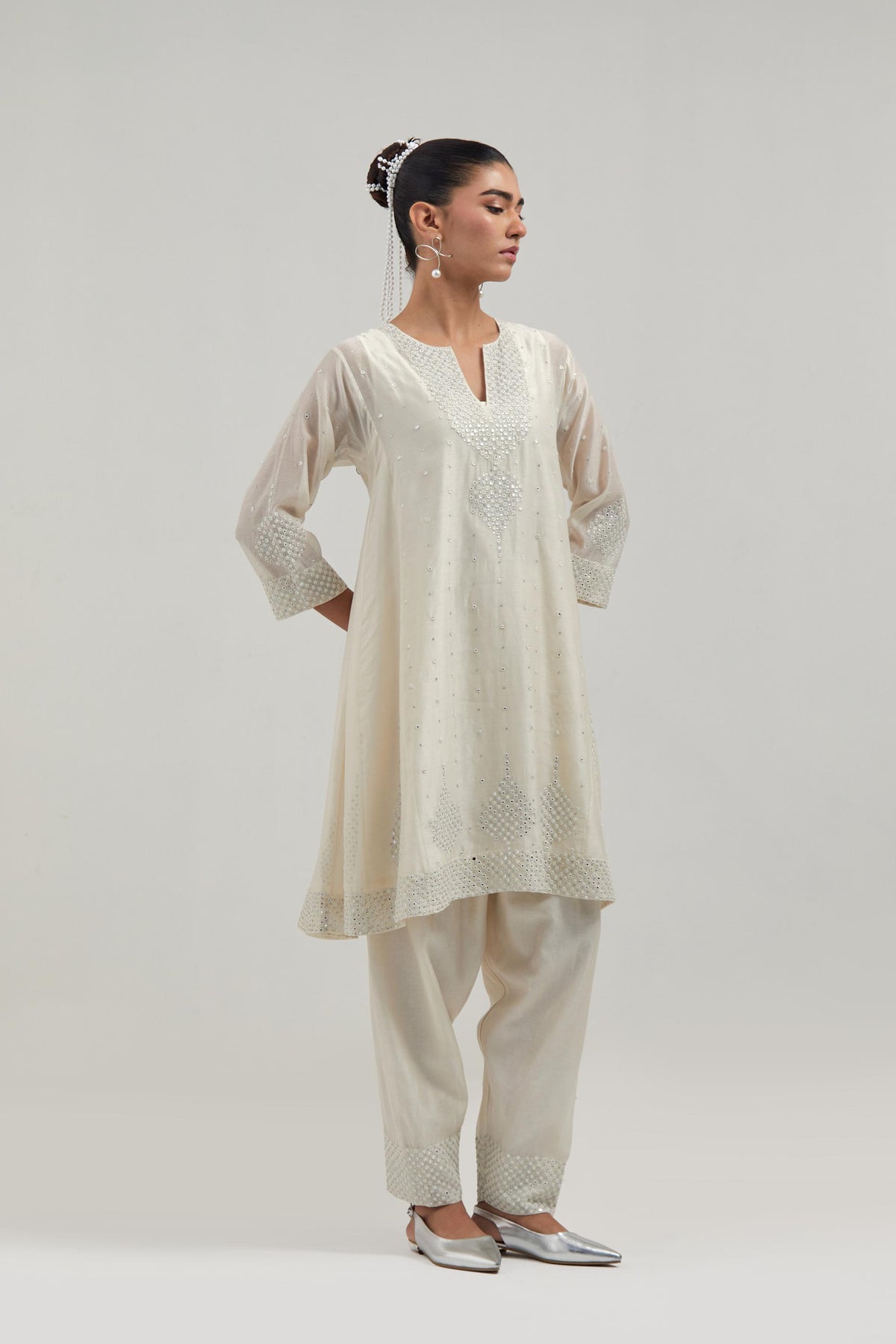 Off white silk Chanderi short kalidar kurta set, with hand embroidered mirror at neck, hem and sleeve edges, highlighted with scattered silver sequins and mirror embellishments all-over.