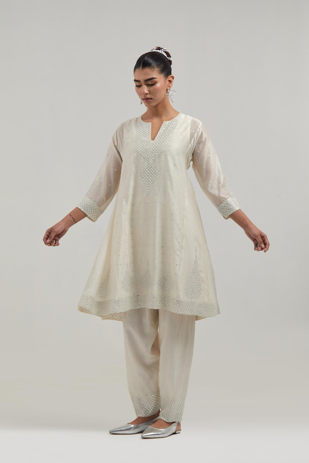 Off white silk Chanderi short kalidar kurta set, with hand embroidered mirror at neck, hem and sleeve edges, highlighted with scattered silver sequins and mirror embellishments all-over.