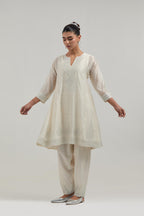 Off white silk Chanderi short kalidar kurta set, with hand embroidered mirror at neck, hem and sleeve edges, highlighted with scattered silver sequins and mirror embellishments all-over.