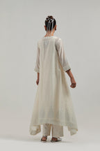 Off-white silk Chanderi kurta set with asymmetric hem and hand-embroidered leaf motifs with delicate mirror and sequins work at the neck, sleeves, and hem, with a mirror border running along the edges.