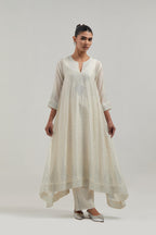 Off-white silk Chanderi kurta set with asymmetric hem and hand-embroidered leaf motifs with delicate mirror and sequins work at the neck, sleeves, and hem, with a mirror border running along the edges.