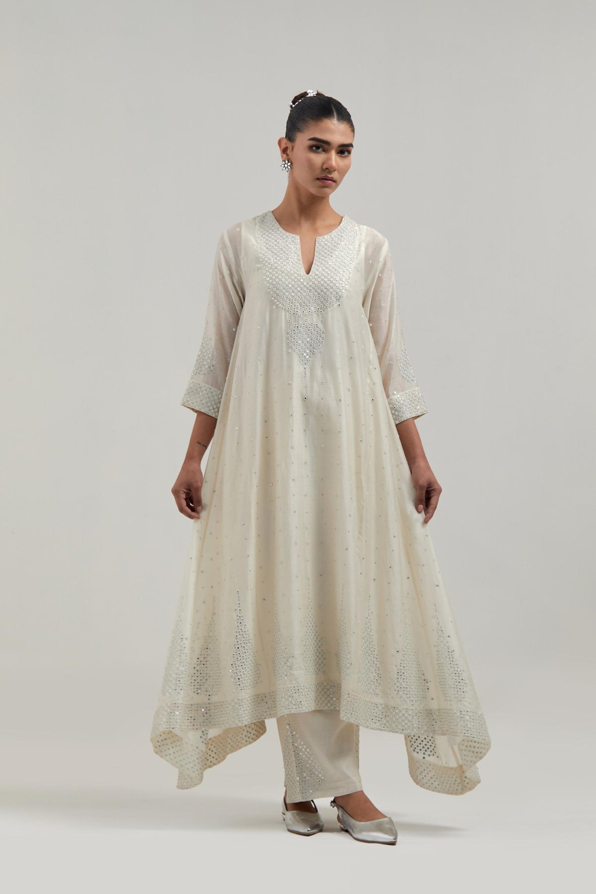Off-white silk Chanderi kurta set with asymmetric hem and hand-embroidered leaf motifs with delicate mirror and sequins work at the neck, sleeves, and hem, with a mirror border running along the edges.