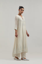 Off-white silk Chanderi kurta set with asymmetric hem and hand-embroidered leaf motifs with delicate mirror and sequins work at the neck, sleeves, and hem, with a mirror border running along the edges.