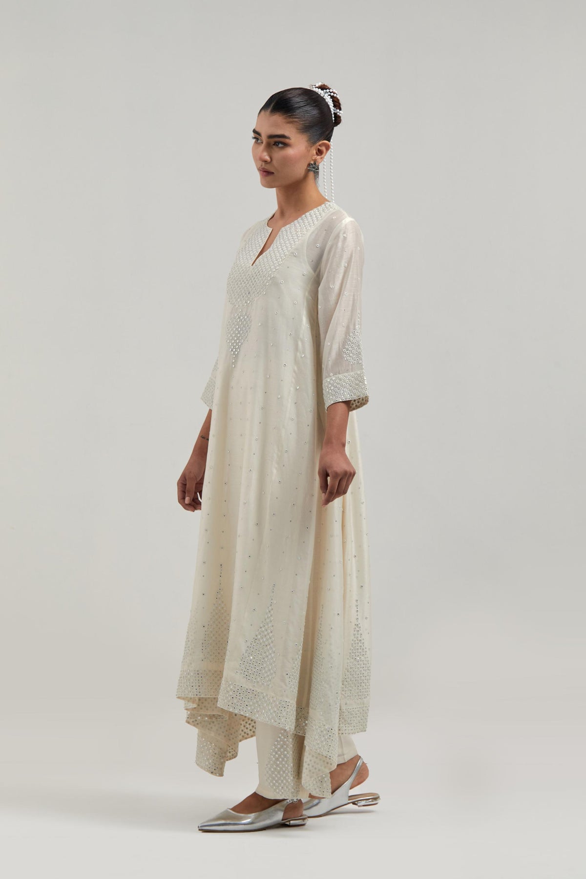 Off-white silk Chanderi kurta set with asymmetric hem and hand-embroidered leaf motifs with delicate mirror and sequins work at the neck, sleeves, and hem, with a mirror border running along the edges.