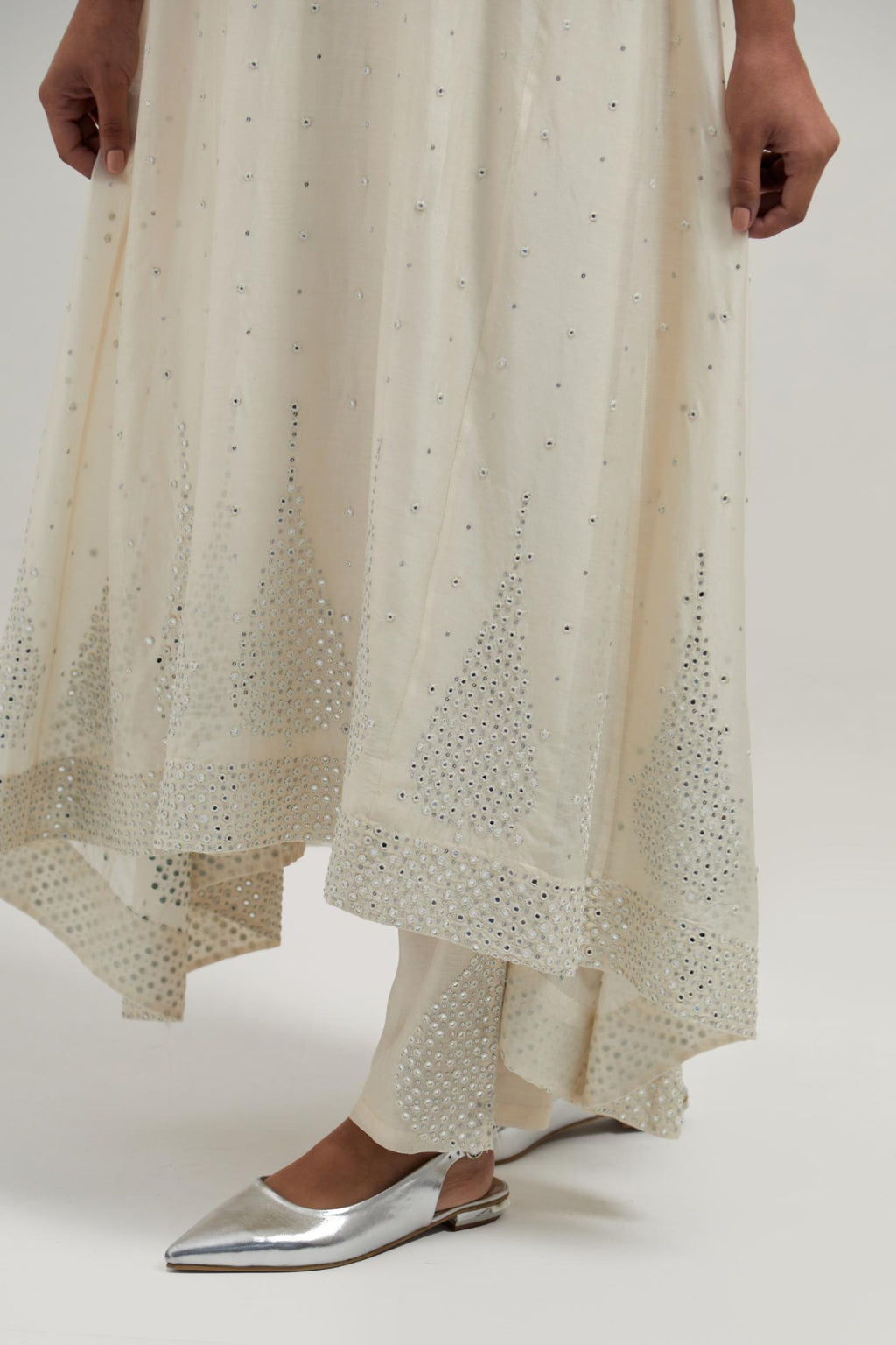 Off-white silk Chanderi kurta set with asymmetric hem and hand-embroidered leaf motifs with delicate mirror and sequins work at the neck, sleeves, and hem, with a mirror border running along the edges.