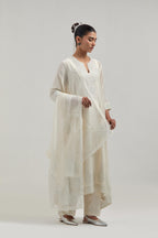 Off-white silk Chanderi kurta set with asymmetric hem and hand-embroidered leaf motifs with delicate mirror and sequins work at the neck, sleeves, and hem, with a mirror border running along the edges.