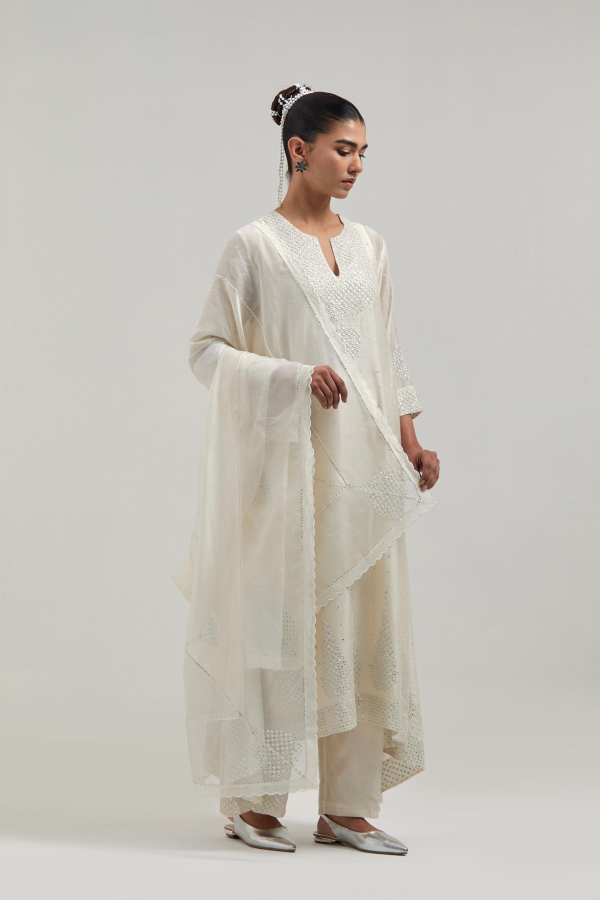 Off-white silk Chanderi kurta set with asymmetric hem and hand-embroidered leaf motifs with delicate mirror and sequins work at the neck, sleeves, and hem, with a mirror border running along the edges.