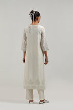 Off white silk Chanderi straight kurta set with hand-embroidered mirror at the neck, borders running along the hem and sleeve edges, and scattered silver sequin and mirror embellishments all-over.