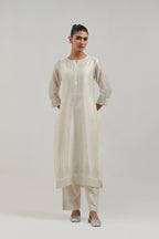 Off white silk Chanderi straight kurta set with hand-embroidered mirror at the neck, borders running along the hem and sleeve edges, and scattered silver sequin and mirror embellishments all-over.