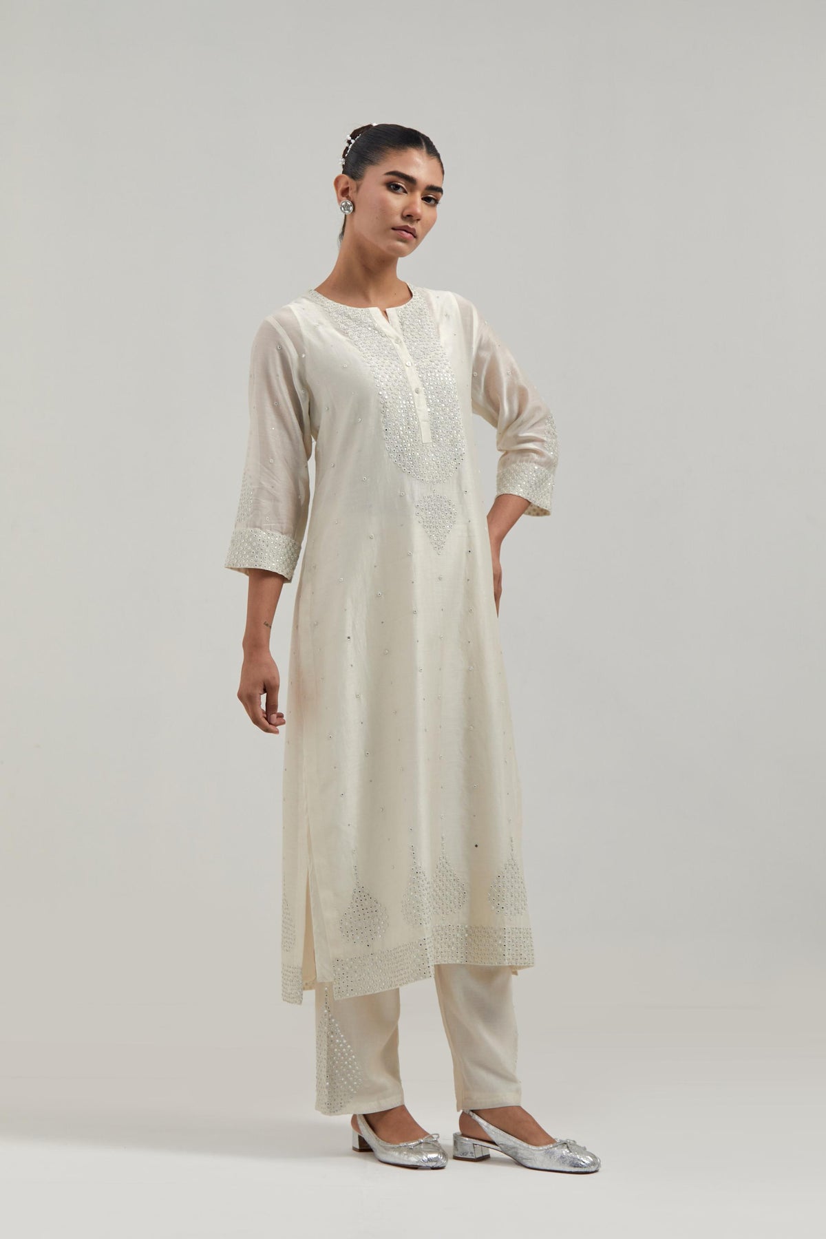 Off white silk Chanderi straight kurta set with hand-embroidered mirror at the neck, borders running along the hem and sleeve edges, and scattered silver sequin and mirror embellishments all-over.