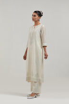 Off white silk Chanderi straight kurta set with hand-embroidered mirror at the neck, borders running along the hem and sleeve edges, and scattered silver sequin and mirror embellishments all-over.