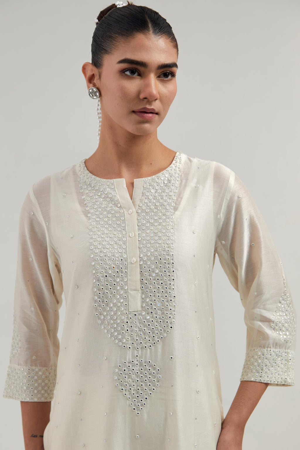 Off white silk Chanderi straight kurta set with hand-embroidered mirror at the neck, borders running along the hem and sleeve edges, and scattered silver sequin and mirror embellishments all-over.