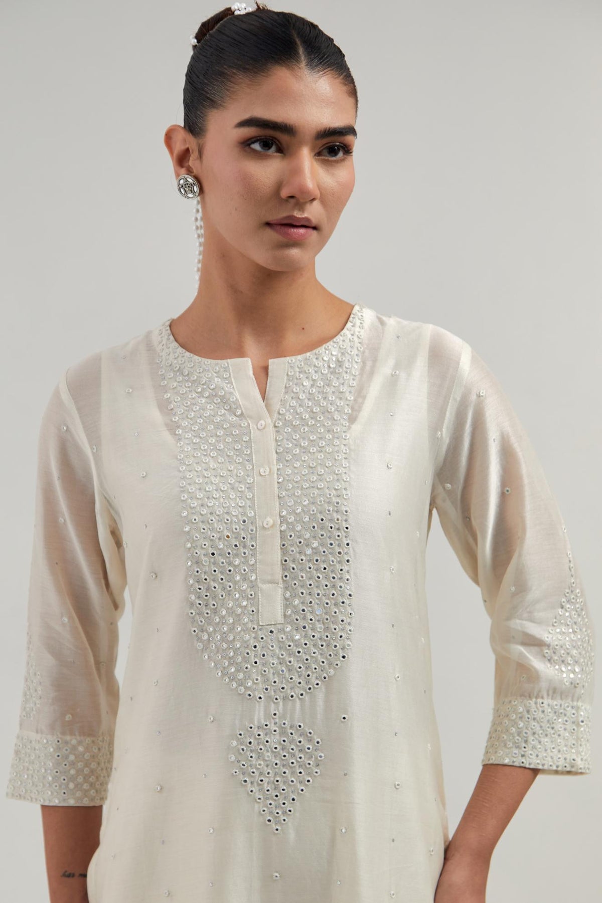 Off white silk Chanderi straight kurta set with hand-embroidered mirror at the neck, borders running along the hem and sleeve edges, and scattered silver sequin and mirror embellishments all-over.