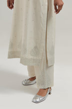 Off white silk Chanderi straight kurta set with hand-embroidered mirror at the neck, borders running along the hem and sleeve edges, and scattered silver sequin and mirror embellishments all-over.