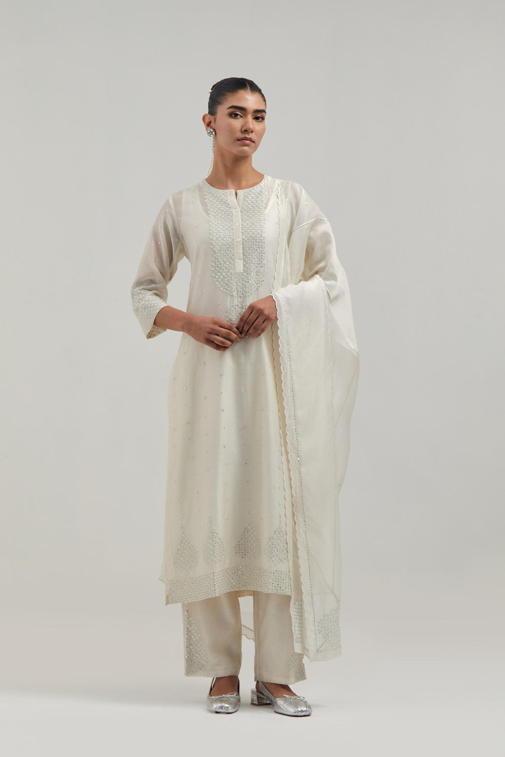 Off white silk Chanderi straight kurta set with hand-embroidered mirror at the neck, borders running along the hem and sleeve edges, and scattered silver sequin and mirror embellishments all-over.