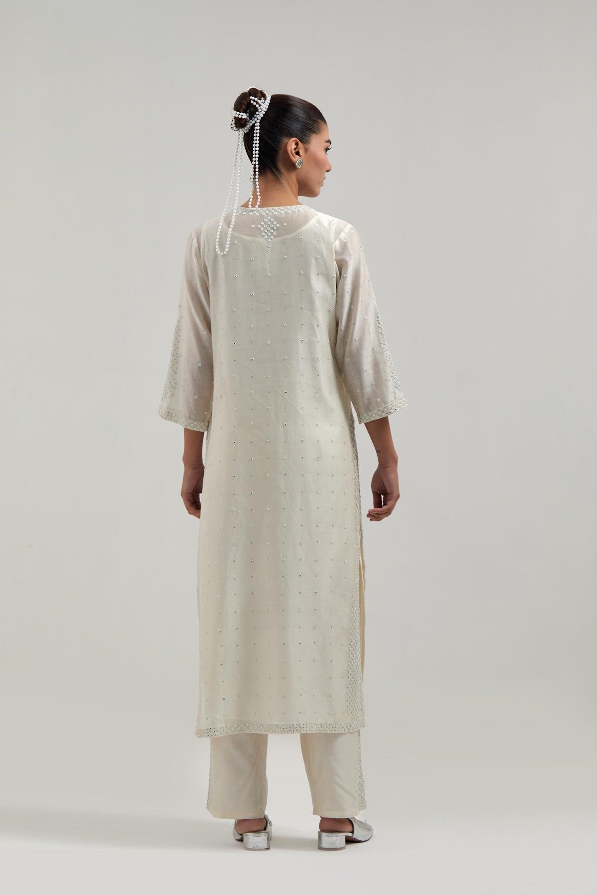 Off white silk Chanderi straight kurta set with hand-embroidered paisley motifs with delicate mirror and sequins work at neck, hem, and sleeves, with narrow borders along the edges.