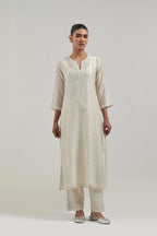 Off white silk Chanderi straight kurta set with hand-embroidered paisley motifs with delicate mirror and sequins work at neck, hem, and sleeves, with narrow borders along the edges.