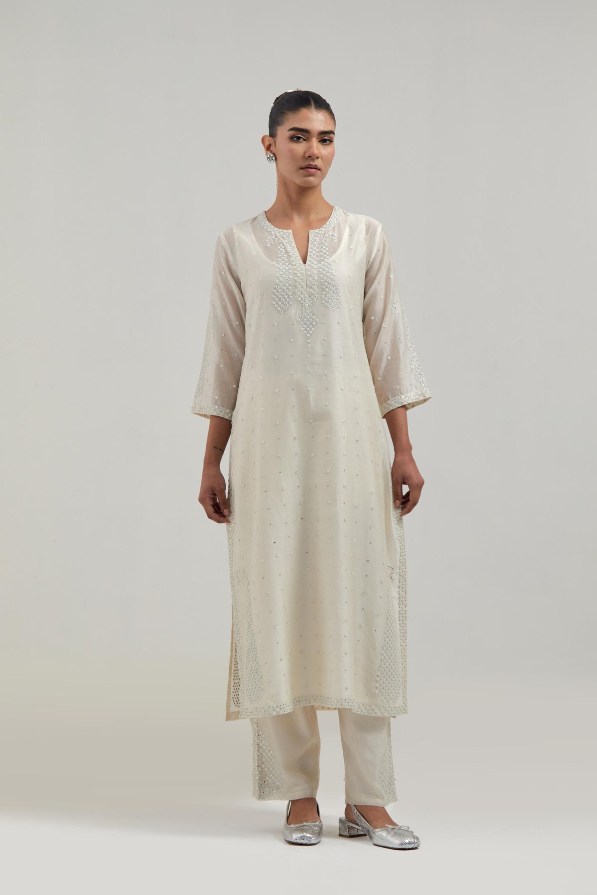 Off white silk Chanderi straight kurta set with hand-embroidered paisley motifs with delicate mirror and sequins work at neck, hem, and sleeves, with narrow borders along the edges.
