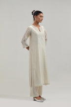 Off white silk Chanderi straight kurta set with hand-embroidered paisley motifs with delicate mirror and sequins work at neck, hem, and sleeves, with narrow borders along the edges.