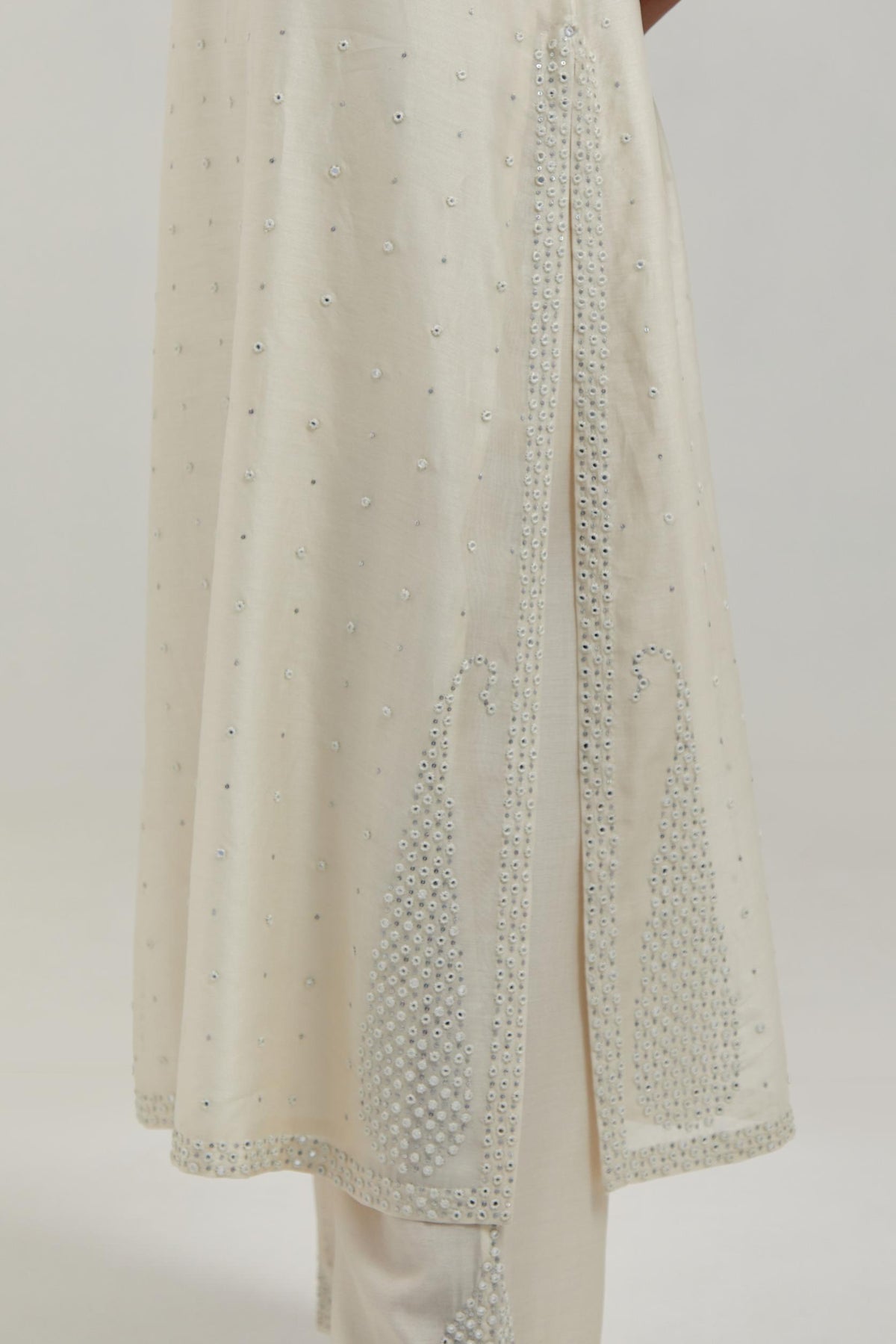 Off white silk Chanderi straight kurta set with hand-embroidered paisley motifs with delicate mirror and sequins work at neck, hem, and sleeves, with narrow borders along the edges.