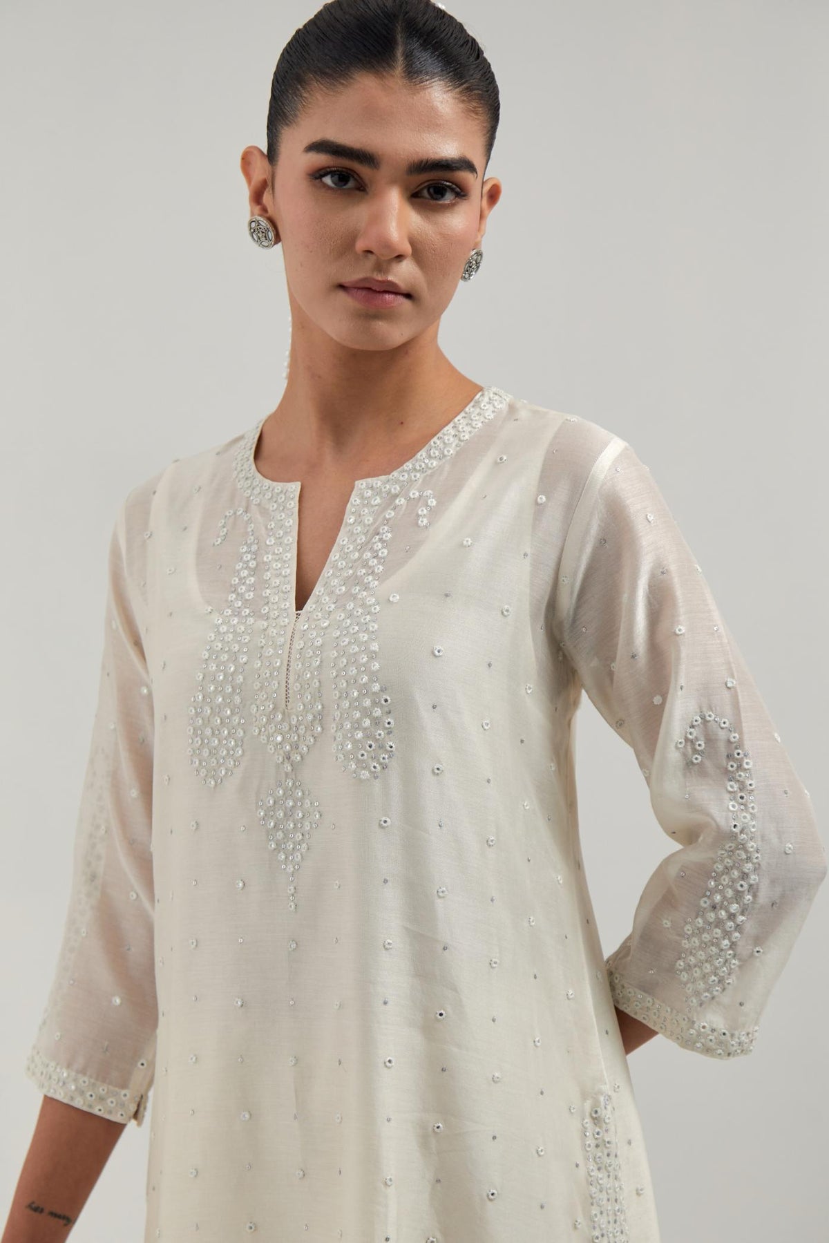 Off white silk Chanderi straight kurta set with hand-embroidered paisley motifs with delicate mirror and sequins work at neck, hem, and sleeves, with narrow borders along the edges.