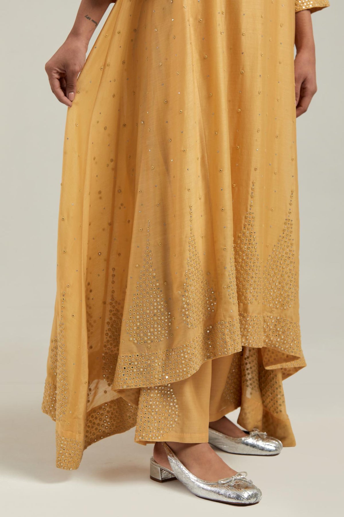 Yellow silk Chanderi kurta set with asymmetric hem and hand-embroidered leaf motifs with delicate mirror and sequins work at the neck, sleeves, and hem, with a mirror border running along the edges.