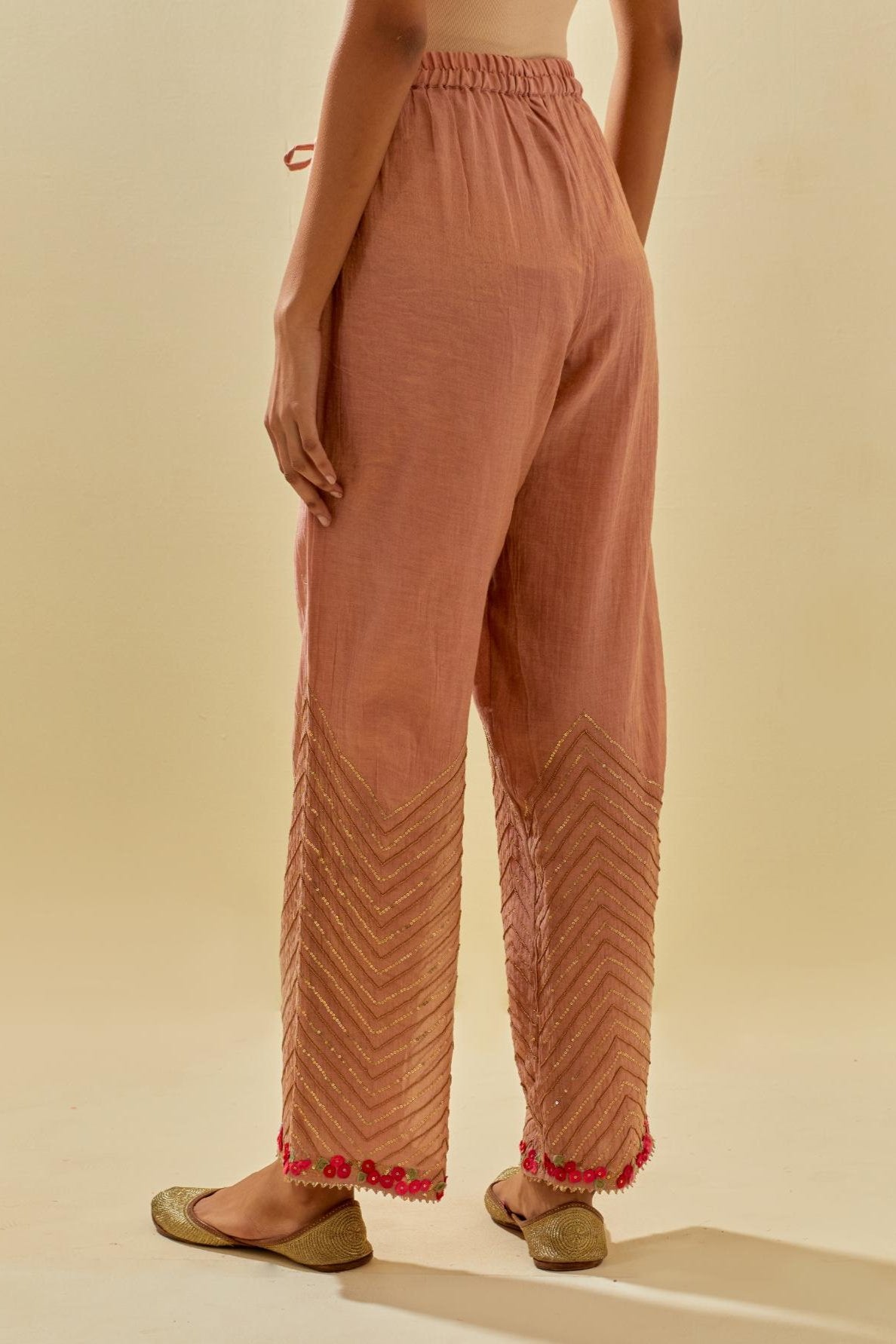 Pink tissue chanderi straight pants with hand cut silk flower embroidery at hem, highlighted with gold sequins and beads.