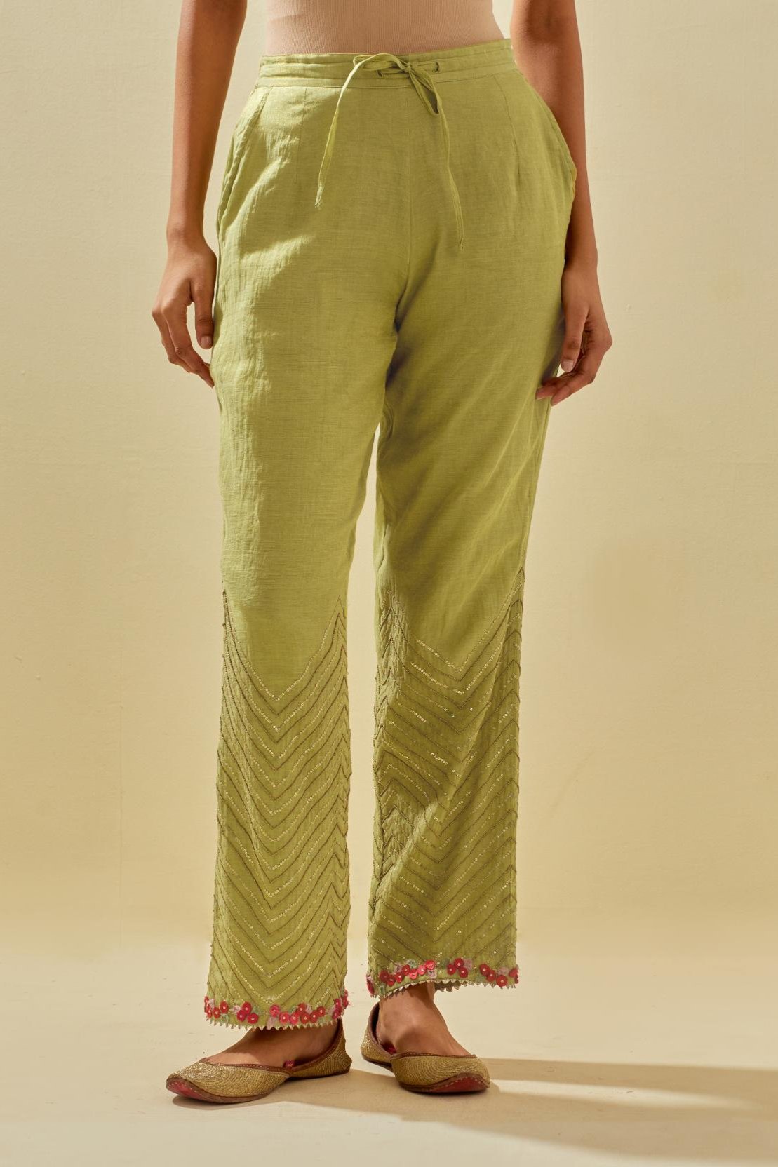 Green tissue chanderi straight pants with hand cut silk flower embroidery at hem, highlighted with gold sequins and beads.
